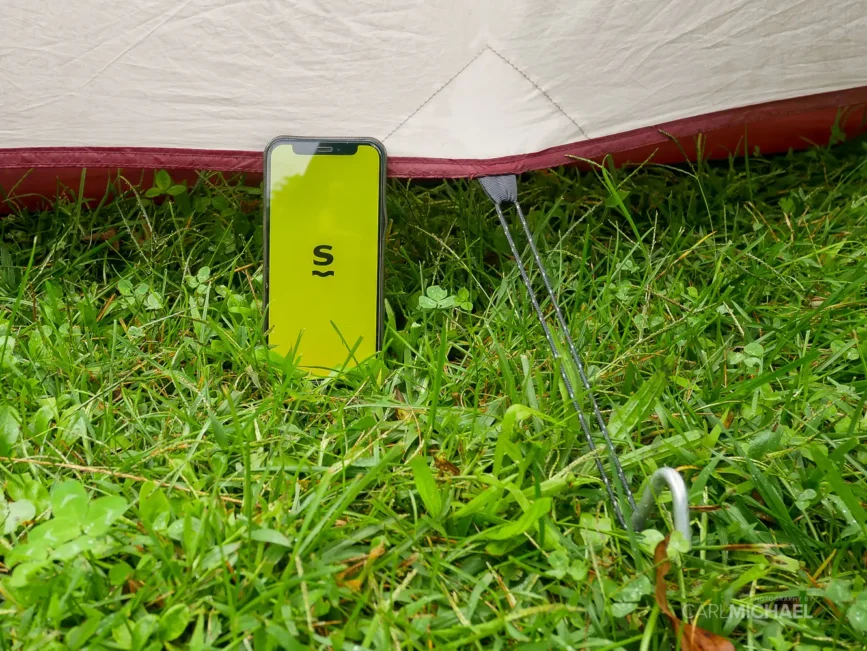Saily eSIM Review: Tested on the Road 5 Mobile phone next to a tent showing Saily eSIM app on screen